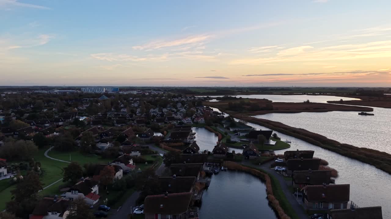 Aerial flyover Dutch holiday resort at the IJsselmeer, with charming waterfront cottages, calm morning light, soft sunrise colors, canals and open water creating a peaceful coastal atmosphere
