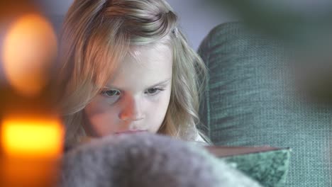 Close-up-of-young-girl’s-face-while-reading-a-book-on-couch