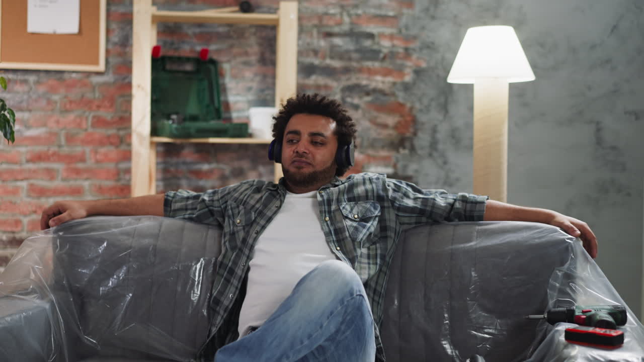 Black man with headphones nods head to music on foiled sofa