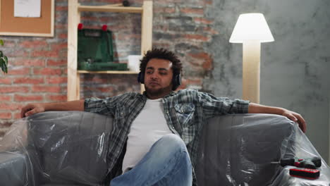 black man with headphones nods head to music on foiled sofa