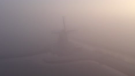 flying backwards away from cornwerder molen windmill during a foggy morning, aerial