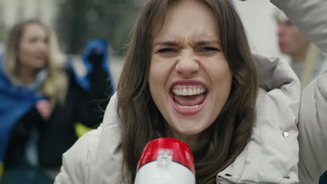 Caucasian-woman-looking-at-camera-and-screaming-through-the-megaphone-in-front-of-manifesting--group-of-young-people.