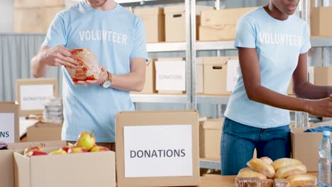 hombre caucásico y joven voluntaria afroamericana empacando cajas de donación con comida en un almacén de caridad