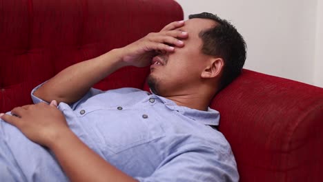 Close-up-of-sad-stressed-middle-aged-asian-man-lying-on-sofa-at-home