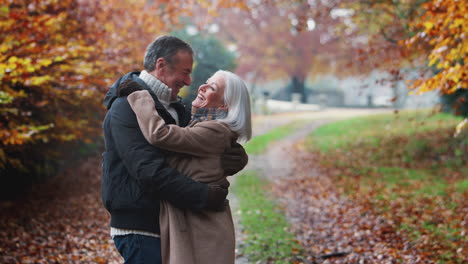 Portrait-Of-Loving-Retired-Senior-Couple-Hugging-Walking-Along-Path-In-Autumn-Countryside