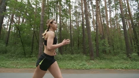 side view of young woman in sports top and shorts running along road in park in morning