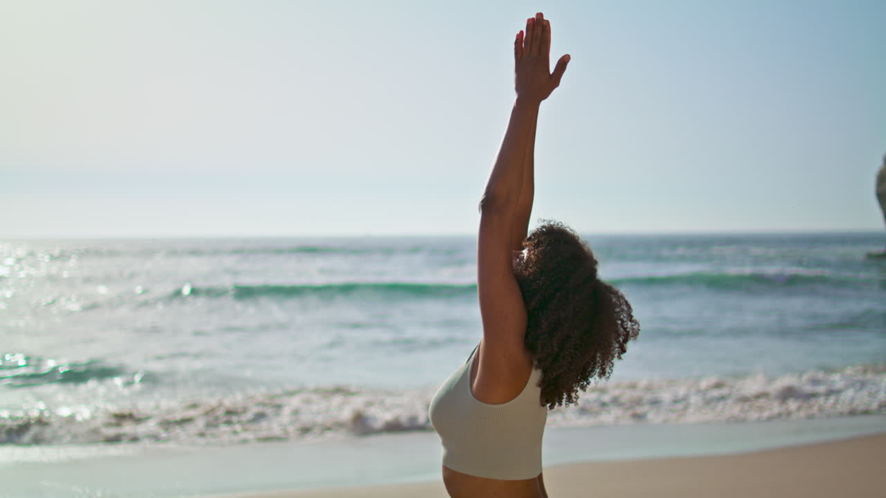 una chica yogi de pie en la arena cerca de las olas del océano haciendo manos de namaste. una mujer meditando.