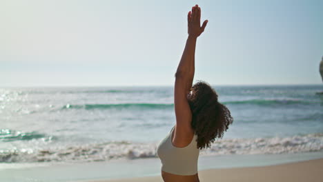 una ragazza yogi in piedi sulla sabbia vicino alle onde dell'oceano che fa le mani di namaste. una donna che medita.