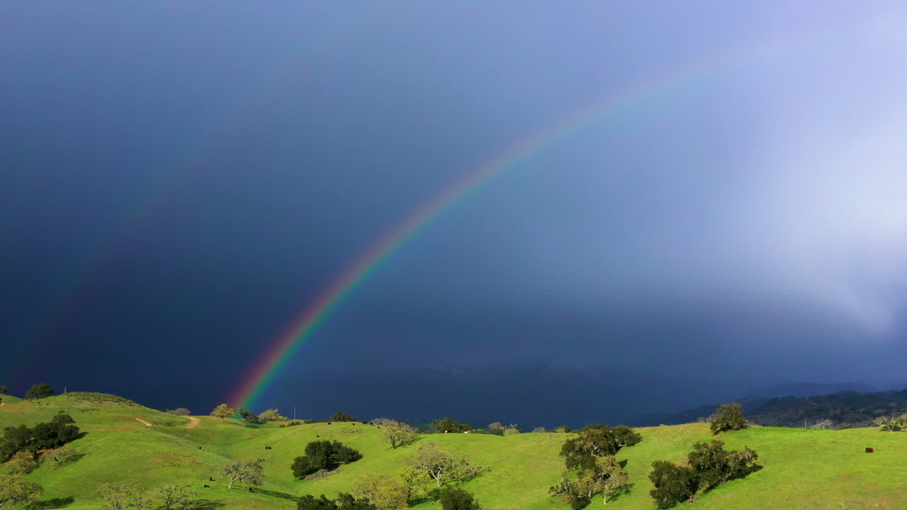 arco iris doble sobre hermosas colinas onduladas con tormenta de nieve en el fondo sobre las montañas
