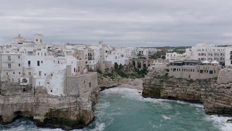 aerial footage pulling out away from the buildings and beach of polignano a mare during a cloudy day in italy