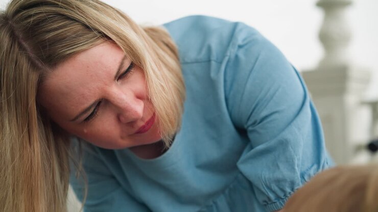 A woman is seen leaning forward, addressing someone in the background, she appears focused, with her attention directed towards the person she's engaging with