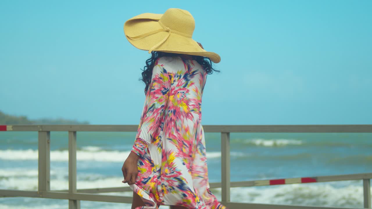 sexy mujer negra camina por la playa con su vestido soplando en el viento revelando un bikini