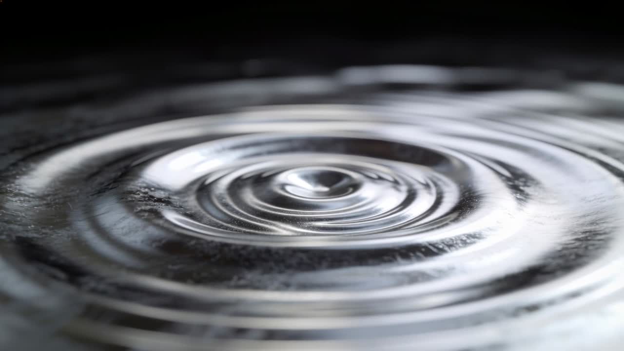 Acqua centrale che increspa formando anelli e un rimbalzo dopo l'impatto in una vasca, mostrando riflessi luminosi.