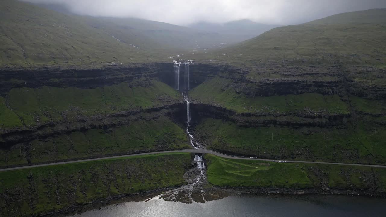 화려한 포사 폭포가 평온한 호수로 흘러들어 가며, 페로 제도의 그림 같은 산 계곡의 휘어지는 도로를 가로질러 흐르며, 자연의 아름다움을 보여줍니다.