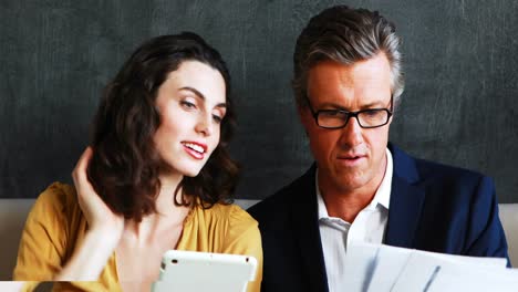 Smiling-businessman-and-colleague-discussing-over-digital-tablet