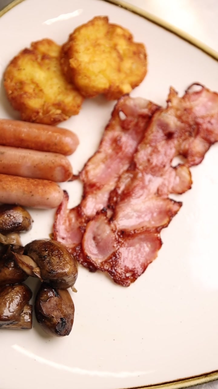 Deliziosa colazione inglese completa con pancetta, salsicce, hash brown e funghi