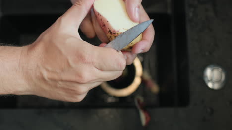 man peels potatoes under running water from a kitchen faucet.