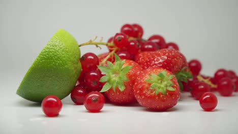 a slice of lime, three sweet strawberries and a bunch of red currants on top of the table - close up shot