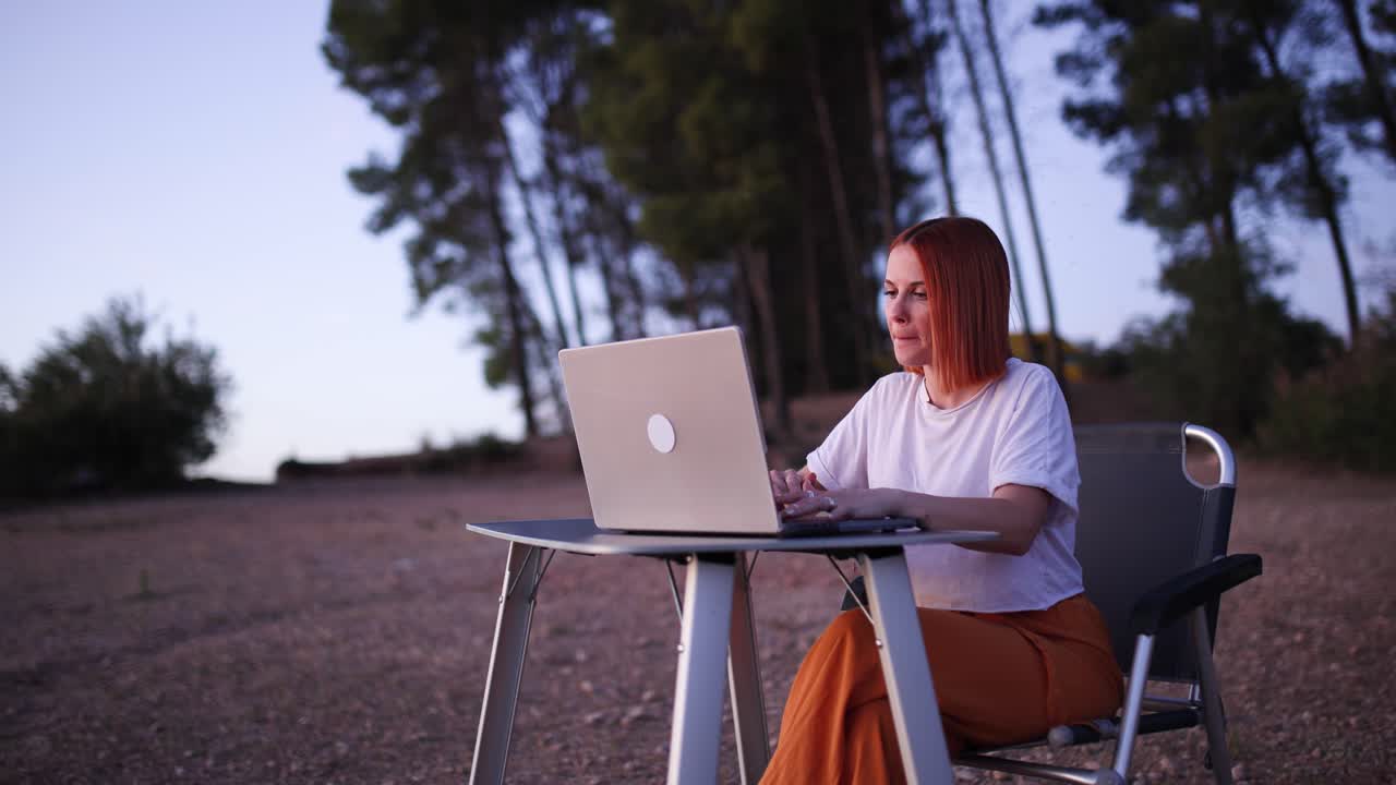 Young Woman Working on Laptop Outdoors at Dusk