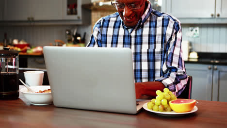 Un-Hombre-Mayor-Sonriente-Usando-Una-Computadora-Portátil-Mientras-Desayuna