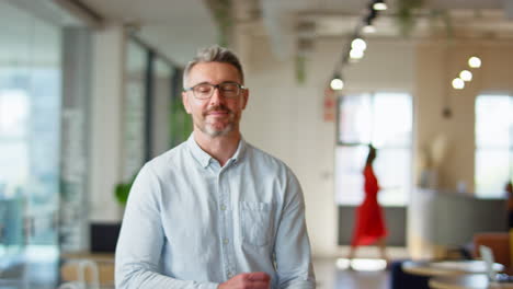 Portrait-Of-Smiling-Mature-Businessman-Standing-In-Modern-Open-Plan-Office