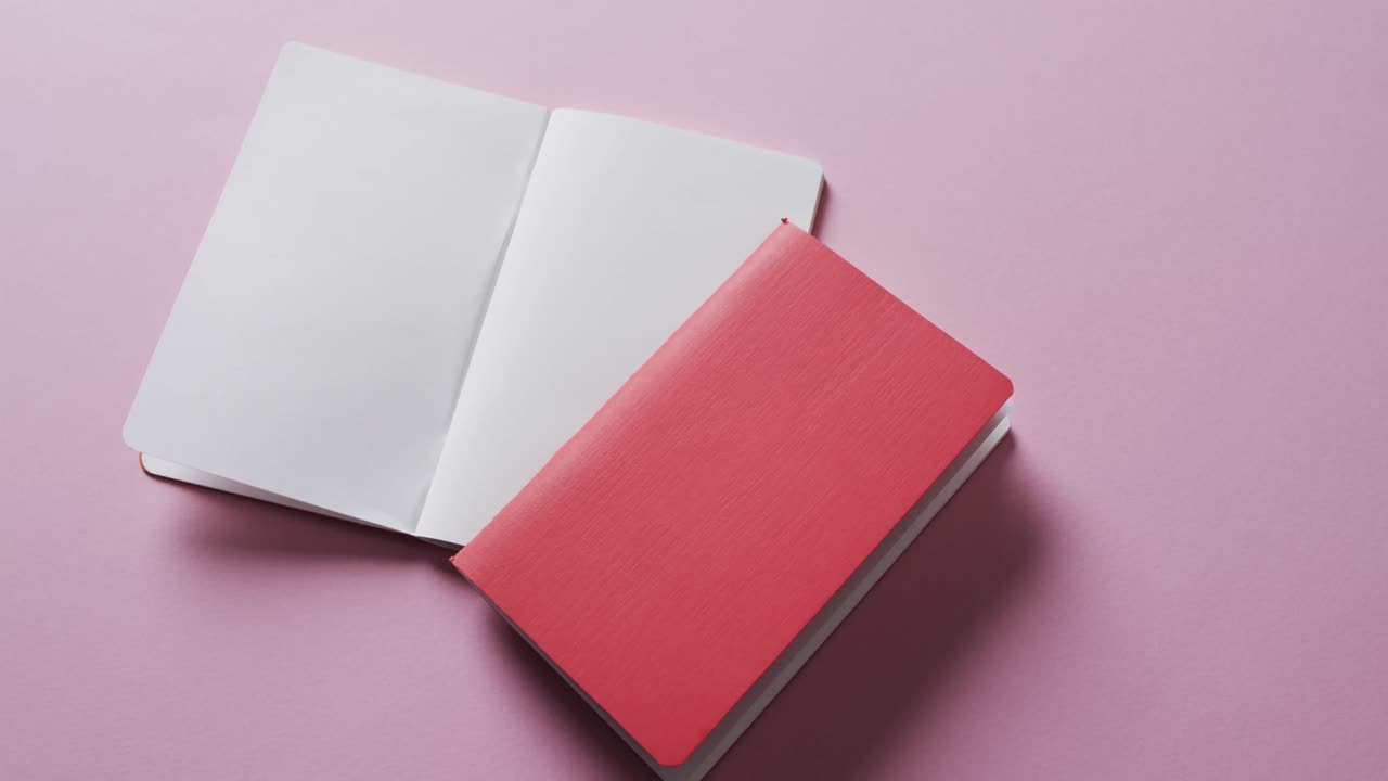 Close up of open blank book and red closed book with copy space on pink background in slow motion