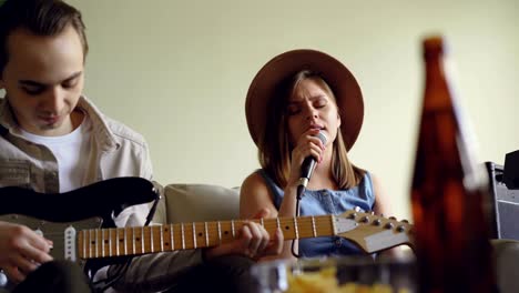 pretty young woman is singing and her handsome friend guitarist is playing the electric guitar during rehearsal in nice light studio. creative duet concept.