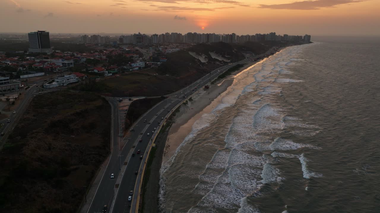 Seaside road traffic by Brazilian city of São Luís at sunset, aerial pull-out