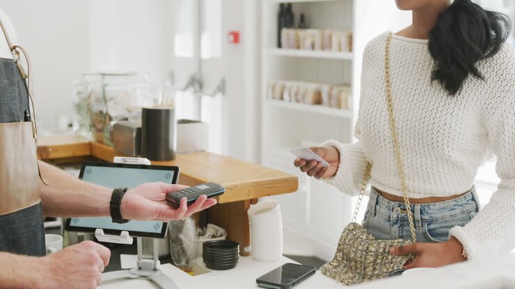 Happy biracial woman paying caucasian male barista with credit card in cafe