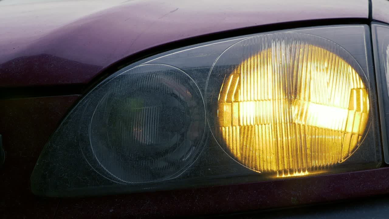 Closeup of a bright shiny headlight with lens flare turns on then off on a dusty red car