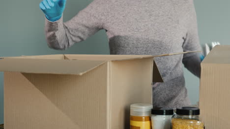 una mujer con guantes protectores empaca alimentos en una caja de cartón para su envío