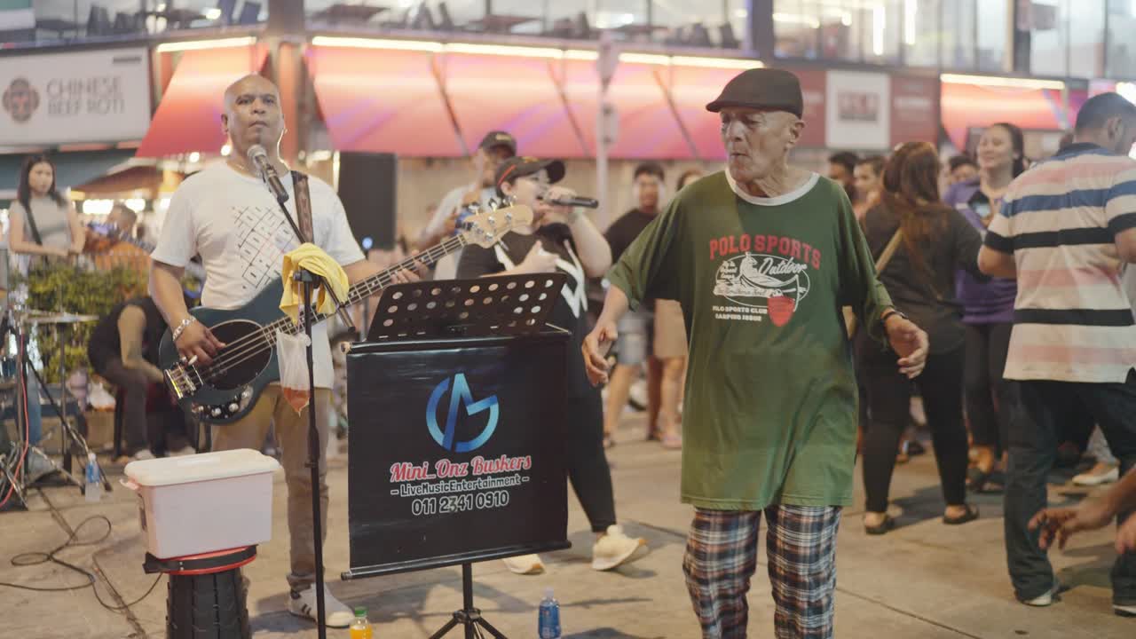 Local buskers performing on Kuala Lumpur streets during nighttime in Malaysia. People enjoying.