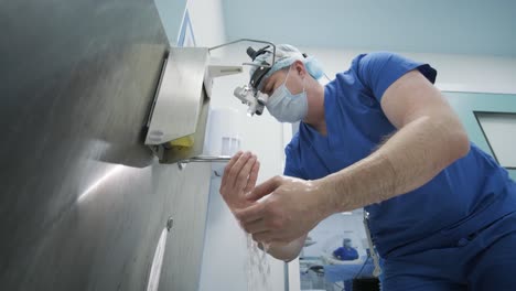 the surgeon prepares for the operation, washes and sterilizes his hands in the modern operating room. doctor is equipped in mask, medical headlamp, surgical loupes