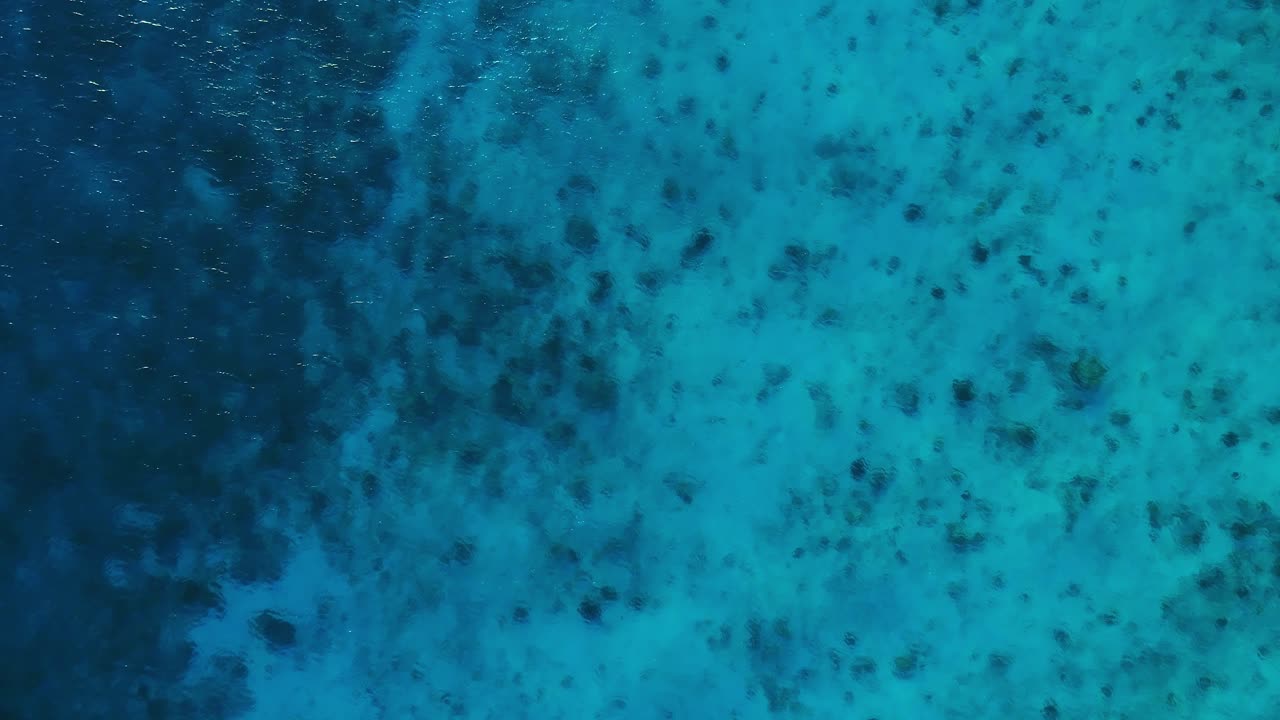 crystal clear turquoise Caribbean sea drop-off to deep blue coral, drone rising, bird's eye view