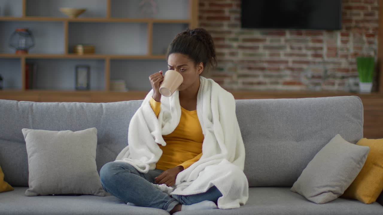 Woman with a blanket on a couch drinking tea.