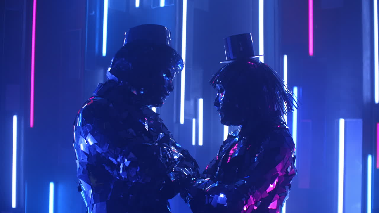 смешные и смешные танцоры покачивают головами в синхронных блестящих костюмах, отражающих свет на неоновой стене.