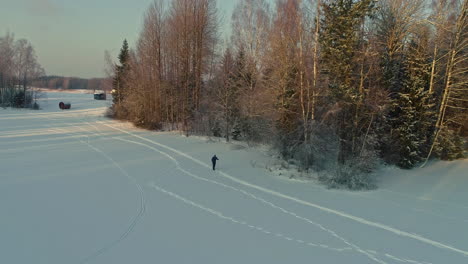 Luftdrohne-Rückwärts-Bewegende-Aufnahme-Eines-Mannes,-Der-Tagsüber-Auf-Weißem-Schnee-Neben-Einem-Nadelwald-Schlittschuh-Läuft