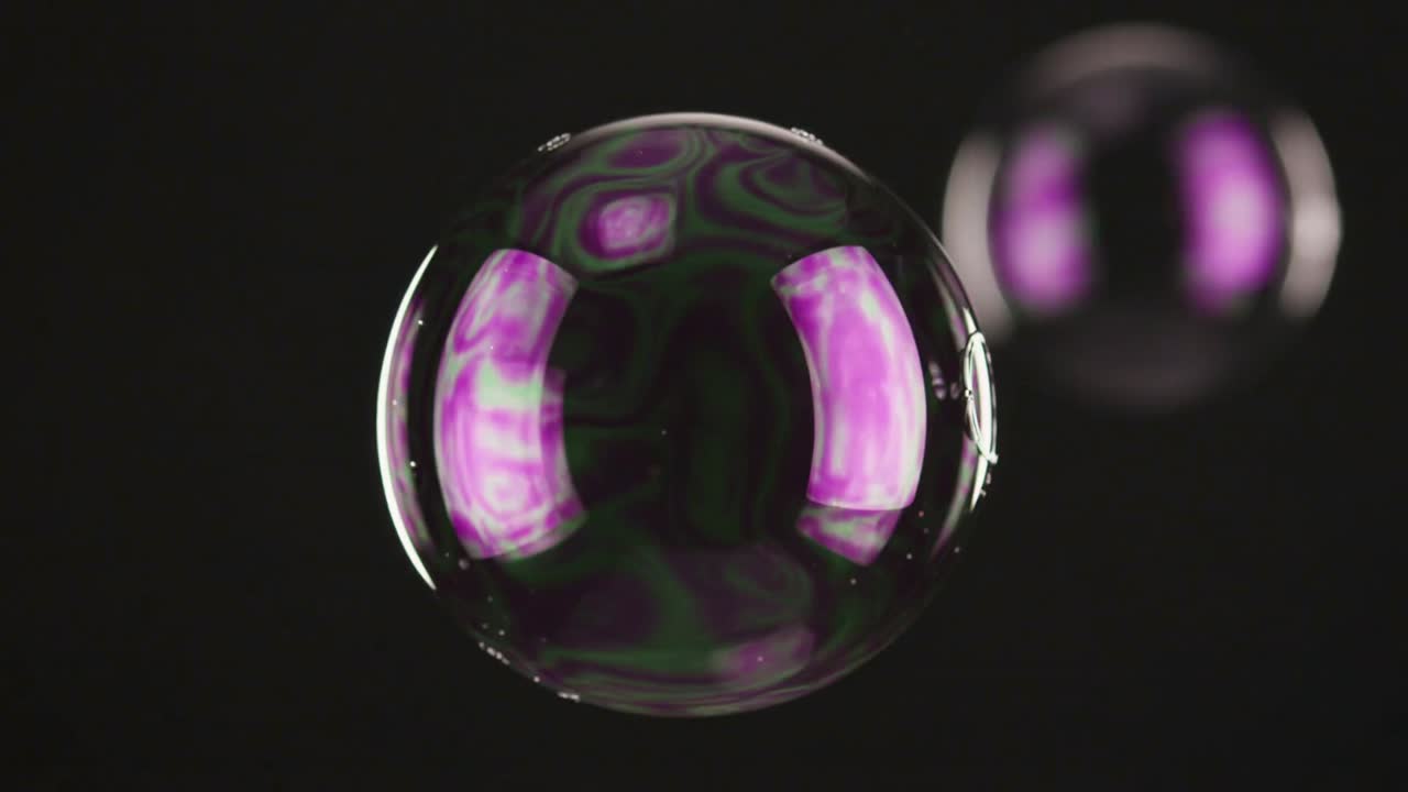 Rotating bubble in studio forming small bubble at rim, popping from film shift, purple panels right