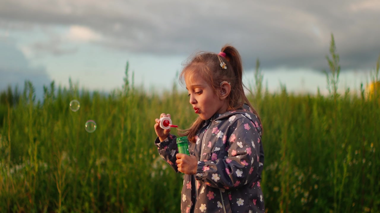 Little Girl Blowing Soap Bubbles in a Green Field