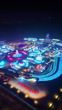vertical drone night shot of harbin ice festival 2025, showcasing vibrant illuminated ice structures, colorful light displays, and a lively winter spectacle. china