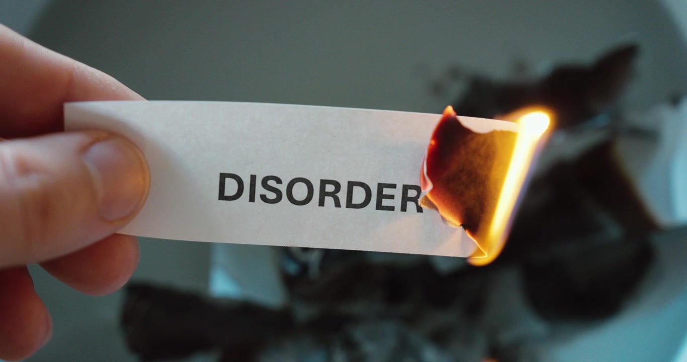 Close-up of a paper strip with the word “disorder” burning, symbolizing overcoming problems, mental health issues, chaos, or personal struggle.