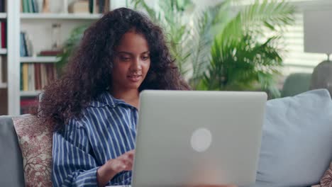 satisfied indian woman using laptop relaxing on comfortable sofa at home