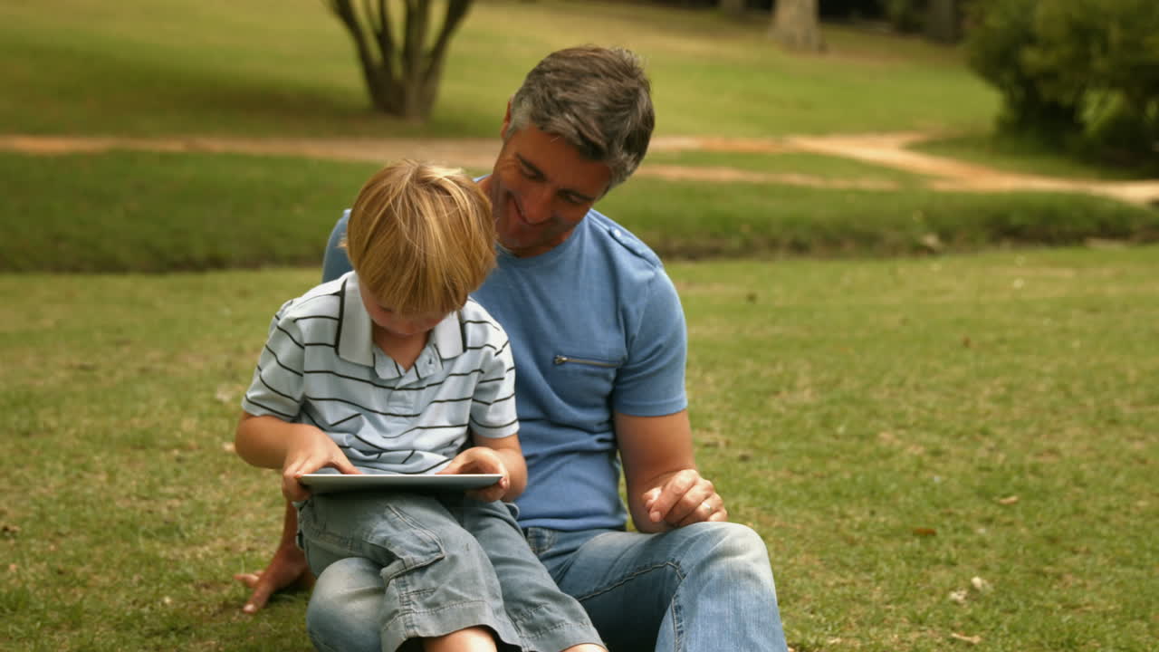 padre feliz con su hijo usando la tableta en el parque