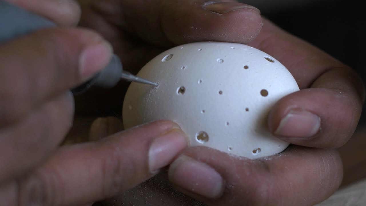 Closeup of a person carving chicken egg using a drill with bare hands