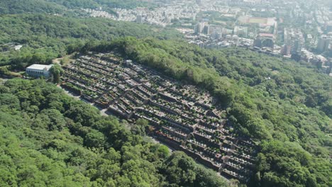 Un-Cementerio-Tradicional-Taiwanés-Ubicado-En-Una-Exuberante-Vegetación-Con-Taipei-Al-Fondo,-Aéreo