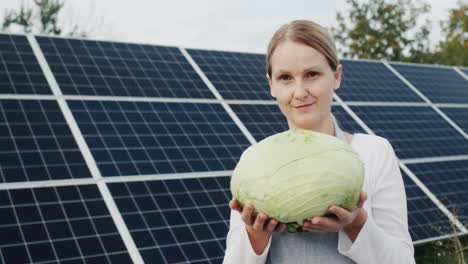Farmer-woman-holding-head-of-cabbage,-standing-against-solar-power-plant-background