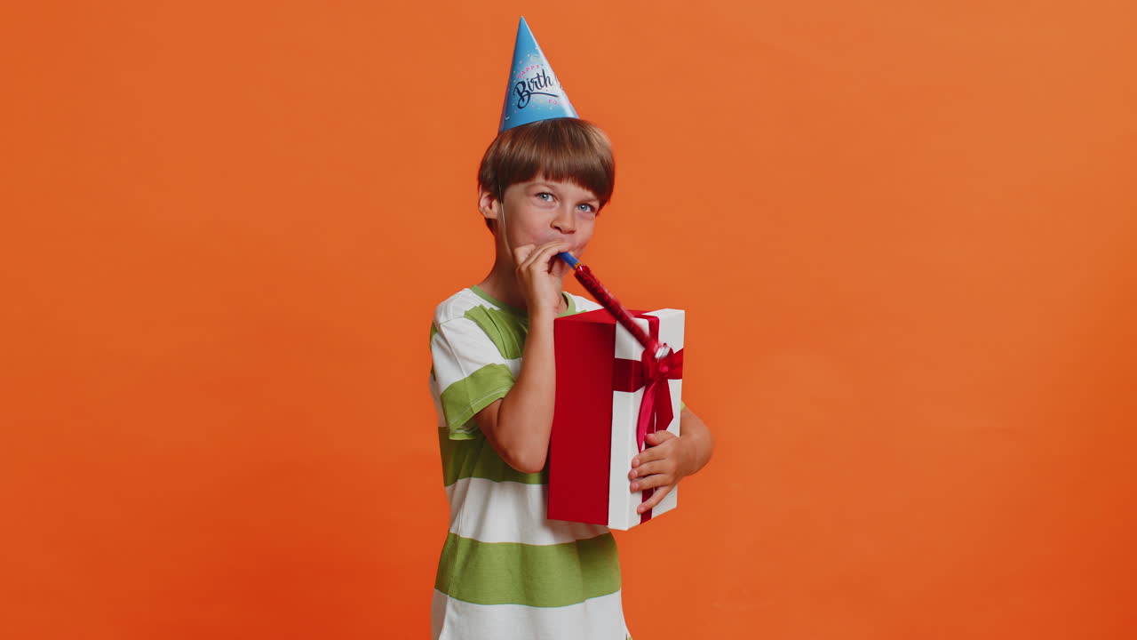 행복하고 흥분한 행운의 소년, 생일 모자를 입고, 파티 성공을 축하하고, 승리를 거두고, 파이프를 불어넣습니다.