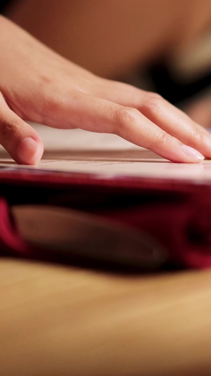A hand gently turns pages of a menu in warm ambient light, suggesting a relaxed dining atmosphere