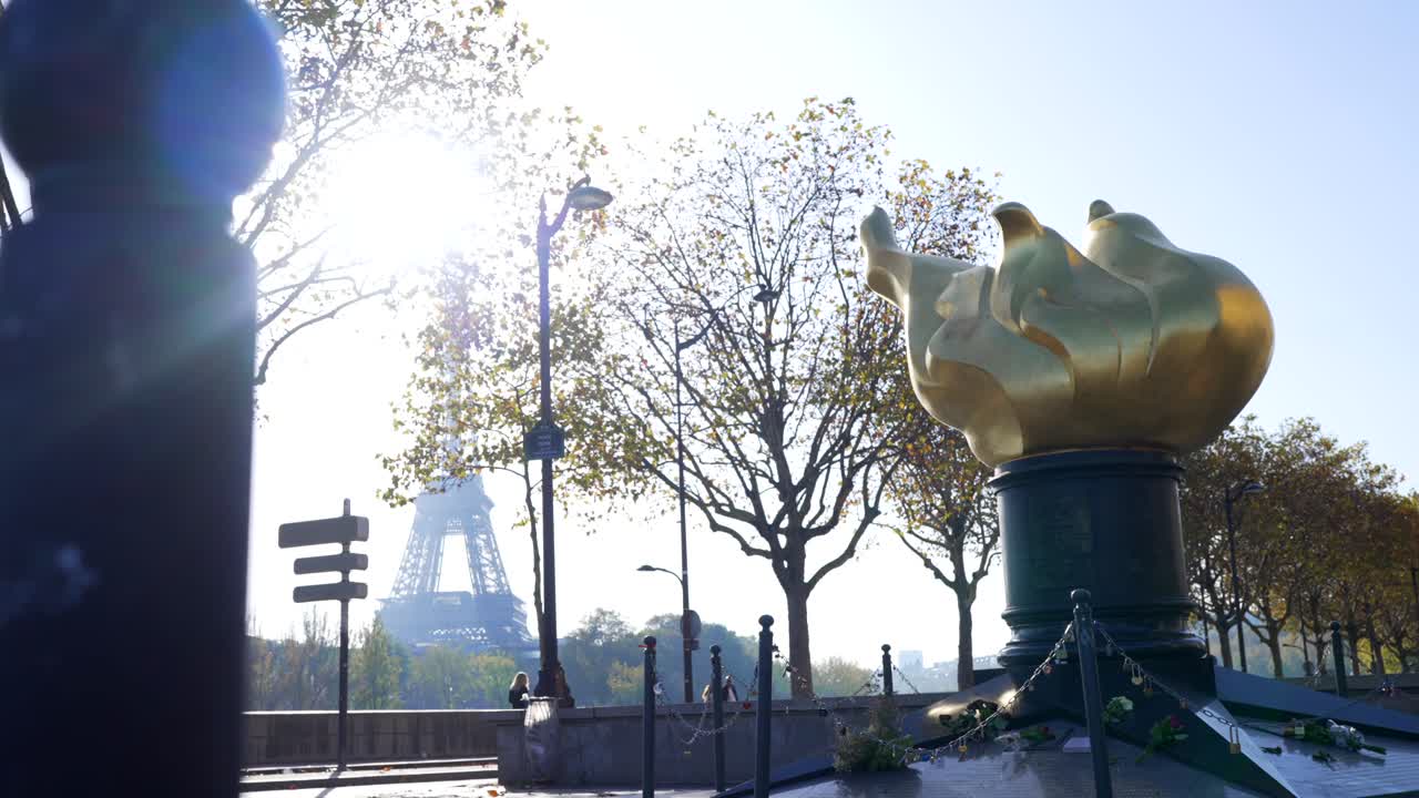 Golden Olympic flame statue in Paris with Eiffel Tower in the background, in bright sunlight, in slow motion