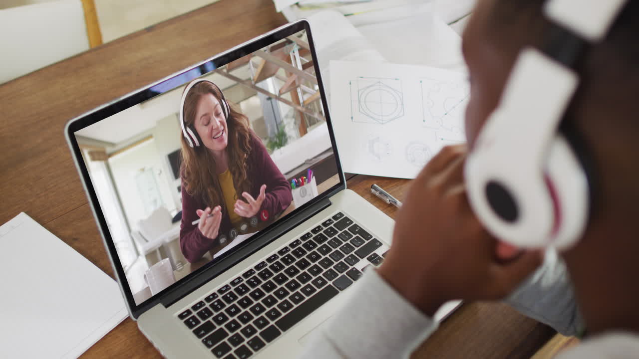 African american male college student holding notes while having a video call on laptop at home